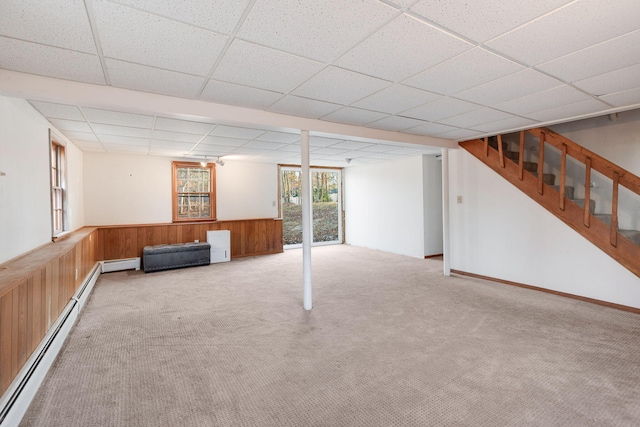 below grade area with baseboard heating, stairway, wooden walls, and a wainscoted wall