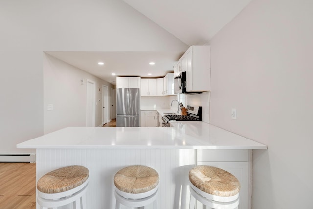 kitchen with lofted ceiling, light countertops, baseboard heating, and stainless steel appliances