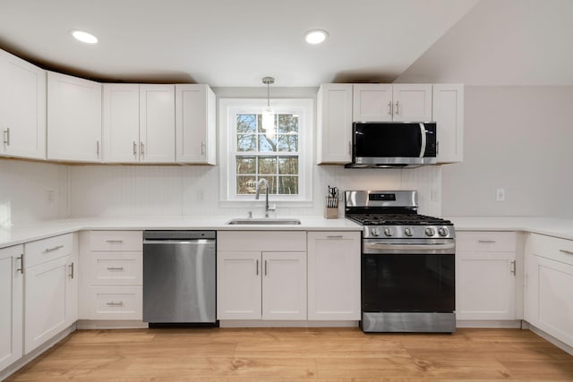 kitchen featuring light wood finished floors, light countertops, appliances with stainless steel finishes, white cabinets, and a sink