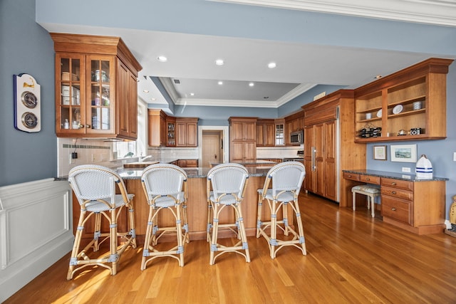 kitchen with brown cabinetry, stainless steel microwave, ornamental molding, a peninsula, and light wood-type flooring