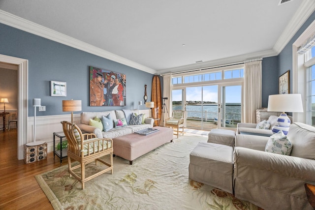 living area featuring ornamental molding, wood finished floors, plenty of natural light, a water view, and a wainscoted wall