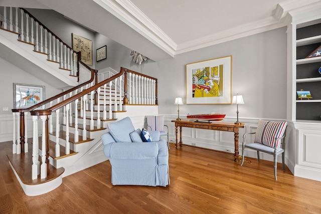 living area featuring crown molding, wood finished floors, stairway, a wainscoted wall, and a decorative wall