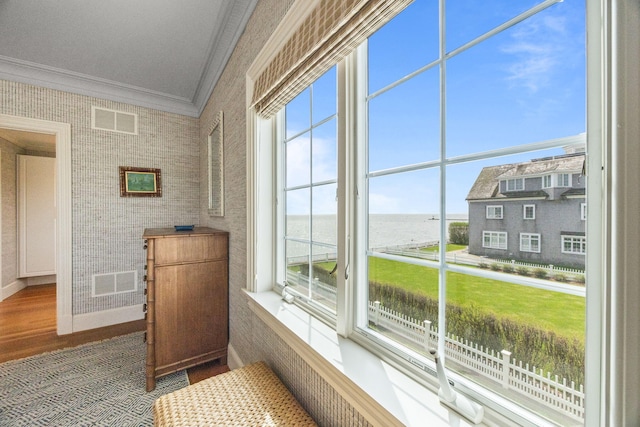 interior space featuring crown molding, a water view, wood finished floors, and baseboards