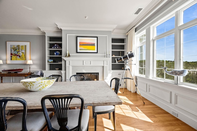 dining area featuring ornamental molding, light wood-type flooring, a fireplace, and built in features