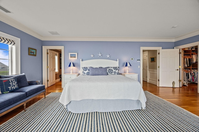 bedroom featuring ornamental molding, wood finished floors, and a spacious closet