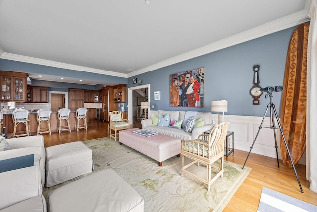 living room featuring light wood-style floors, crown molding, and wainscoting