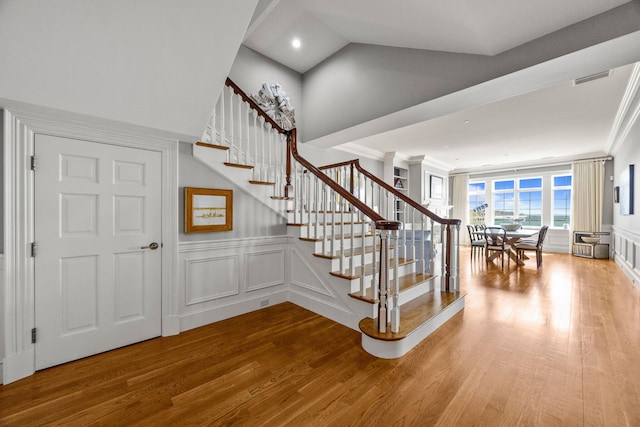 stairs featuring wood finished floors, a decorative wall, ornamental molding, and wainscoting