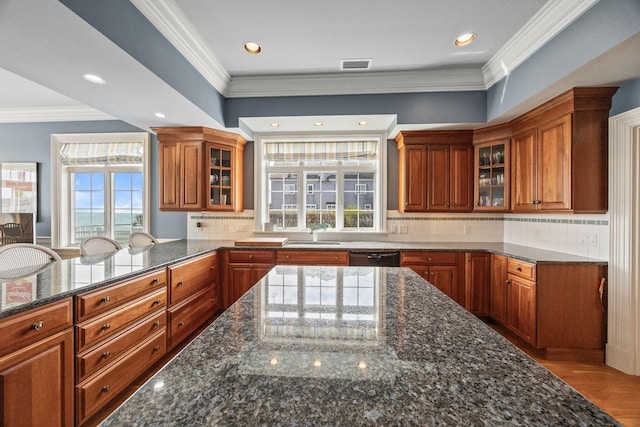 kitchen featuring brown cabinets, a sink, dark stone counters, glass insert cabinets, and ornamental molding