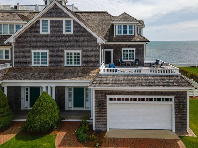 shingle-style home with a water view, driveway, a balcony, and a garage