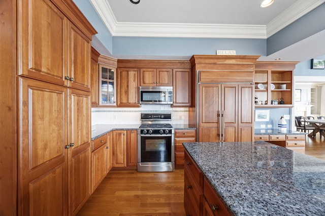 kitchen featuring stainless steel appliances, open shelves, dark wood-style flooring, dark stone counters, and crown molding