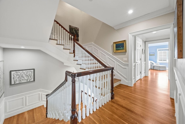 staircase with a decorative wall, crown molding, wood finished floors, a wainscoted wall, and recessed lighting