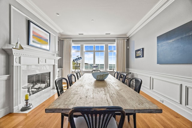 dining area with crown molding, wood finished floors, a premium fireplace, and a wainscoted wall