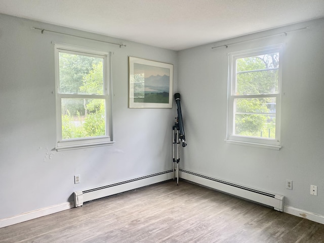 spare room with hardwood / wood-style floors, plenty of natural light, and a baseboard heating unit