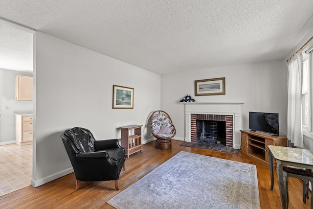 living room with a textured ceiling, baseboards, a brick fireplace, and wood finished floors