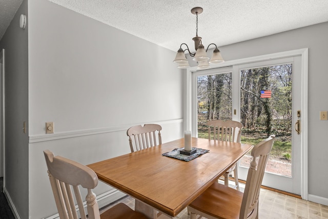 dining space with baseboards, a textured ceiling, and a chandelier