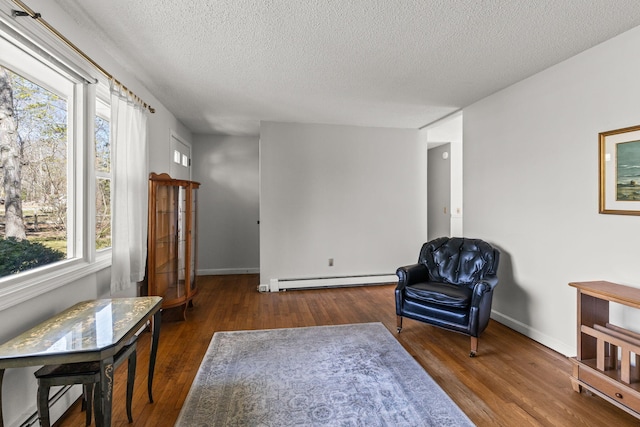 living area with a textured ceiling, baseboards, baseboard heating, and wood finished floors