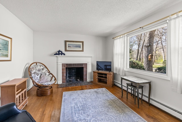 living area featuring wood finished floors, a textured ceiling, a brick fireplace, and a baseboard heating unit
