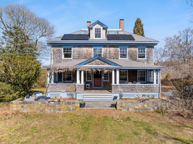 shingle-style home with a porch, a front lawn, a chimney, and solar panels
