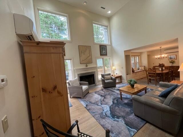 living room with a high ceiling, an inviting chandelier, light hardwood / wood-style floors, and a wall mounted AC