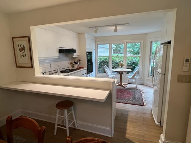 kitchen featuring light hardwood / wood-style floors, tasteful backsplash, white fridge, white cabinets, and kitchen peninsula