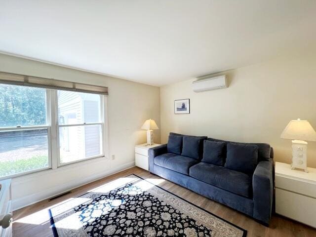 living room with an AC wall unit, light hardwood / wood-style floors, and a healthy amount of sunlight