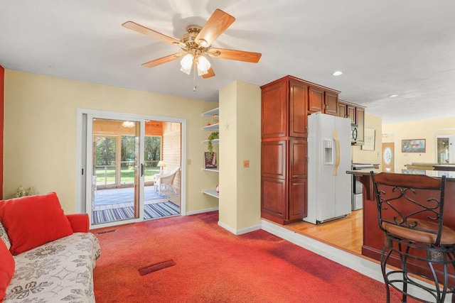 kitchen featuring ceiling fan, white refrigerator with ice dispenser, stove, and light carpet