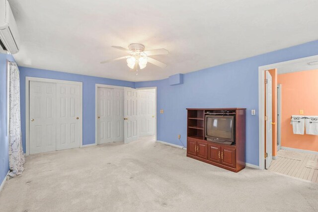 unfurnished bedroom featuring a wall mounted air conditioner, two closets, light colored carpet, ceiling fan, and connected bathroom