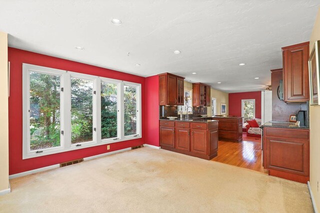 kitchen featuring sink, light colored carpet, kitchen peninsula, and dark stone countertops