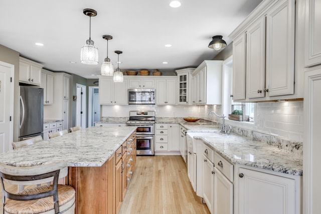 kitchen featuring appliances with stainless steel finishes, white cabinetry, hanging light fixtures, a kitchen island, and backsplash