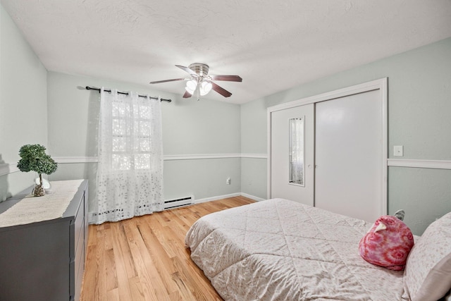 bedroom featuring wood-type flooring, a closet, a baseboard heating unit, and ceiling fan