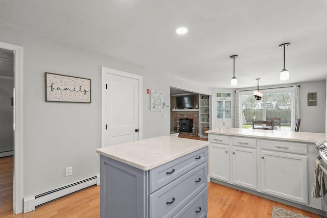 kitchen with a brick fireplace, light wood-style floors, a baseboard heating unit, light stone counters, and hanging light fixtures