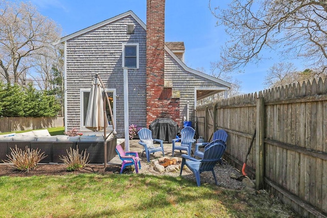 rear view of house with a lawn, a chimney, a fenced backyard, and an outdoor fire pit