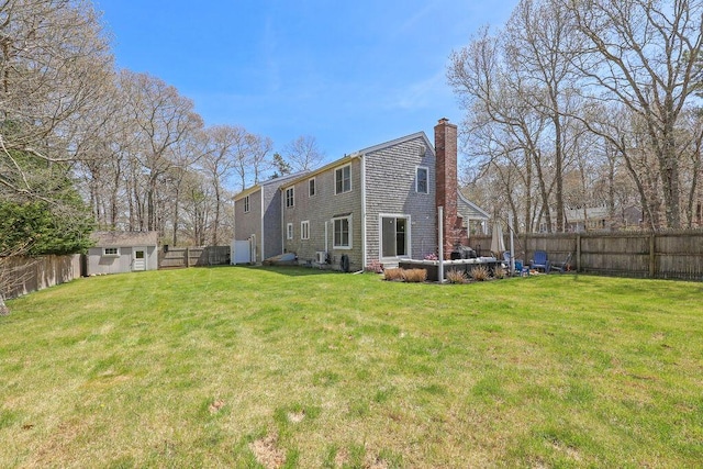 rear view of property featuring a lawn, an outdoor structure, a chimney, and a fenced backyard