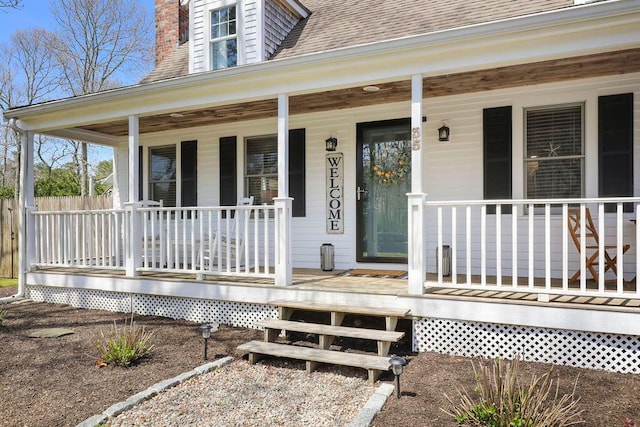 view of exterior entry with a porch, fence, a shingled roof, and a chimney