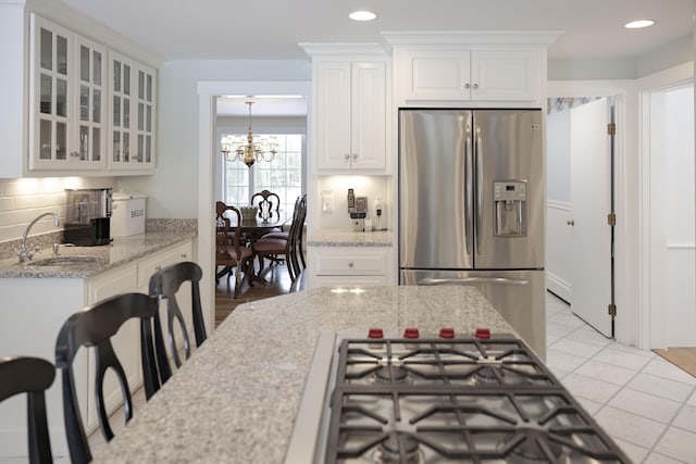 kitchen featuring sink, appliances with stainless steel finishes, light stone countertops, decorative backsplash, and white cabinets