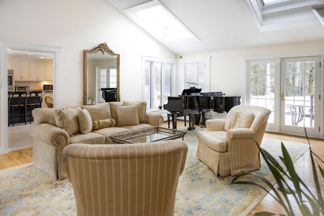 living room featuring french doors, a skylight, high vaulted ceiling, and light hardwood / wood-style flooring