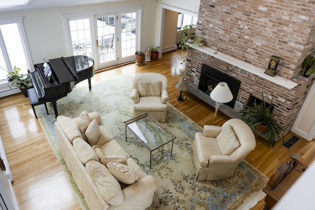 living room with a brick fireplace, a baseboard heating unit, and light wood-type flooring