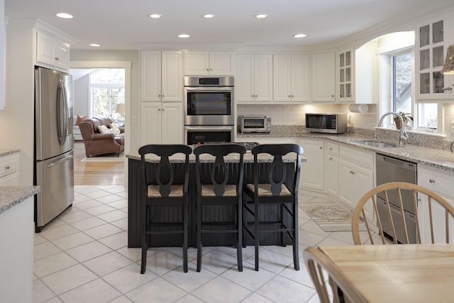 kitchen with a breakfast bar, sink, light stone counters, stainless steel appliances, and white cabinets