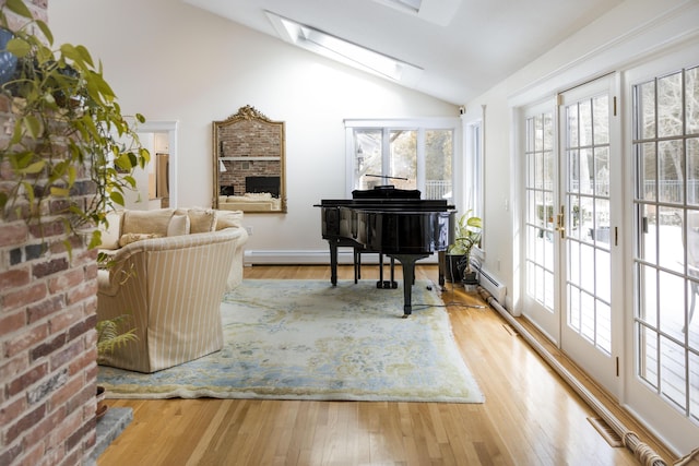 living area featuring a baseboard heating unit, a fireplace, lofted ceiling with skylight, and light wood-type flooring