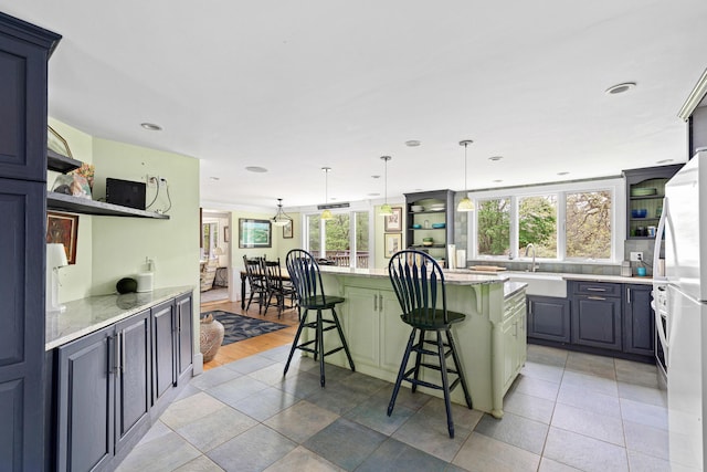 kitchen featuring sink, a breakfast bar, hanging light fixtures, light stone counters, and a kitchen island