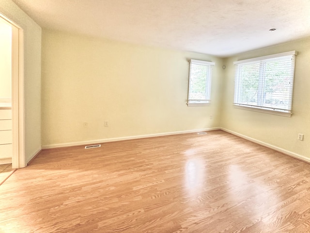 unfurnished room featuring baseboards, light wood-type flooring, and visible vents