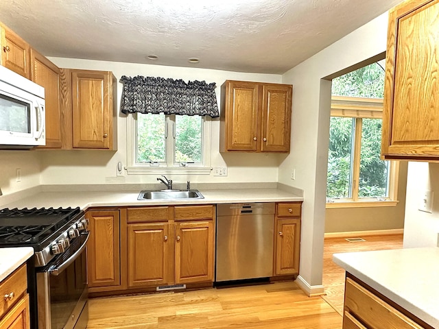 kitchen with sink, light hardwood / wood-style floors, appliances with stainless steel finishes, and a textured ceiling