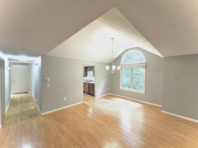 interior space with a textured ceiling, a chandelier, light wood-style flooring, baseboards, and vaulted ceiling