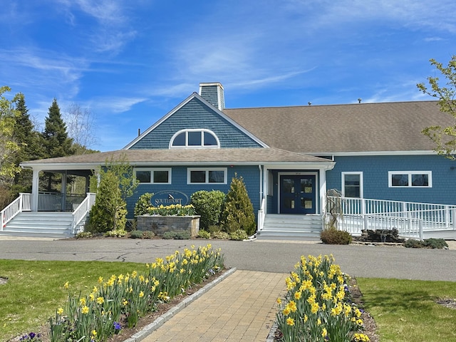 shingle-style home featuring a shingled roof, covered porch, and a chimney