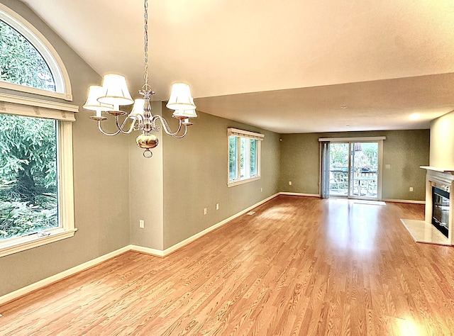 unfurnished living room with light hardwood / wood-style flooring, a notable chandelier, and vaulted ceiling