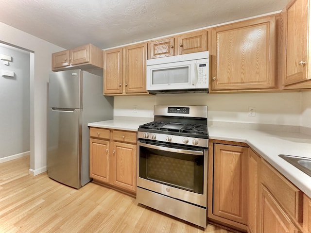 kitchen featuring light countertops, stainless steel appliances, baseboards, and light wood-type flooring