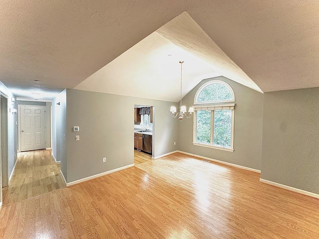 unfurnished living room featuring a textured ceiling, vaulted ceiling, an inviting chandelier, and light wood-type flooring