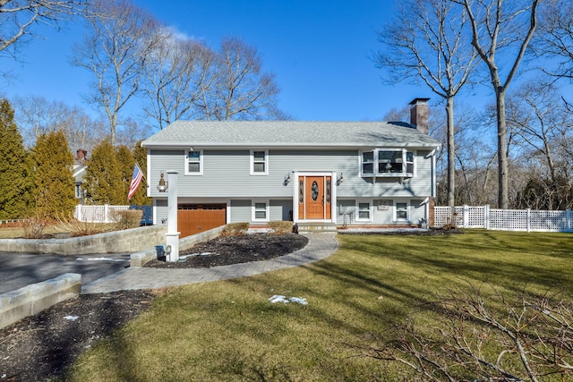 bi-level home with an attached garage, fence, driveway, a chimney, and a front yard