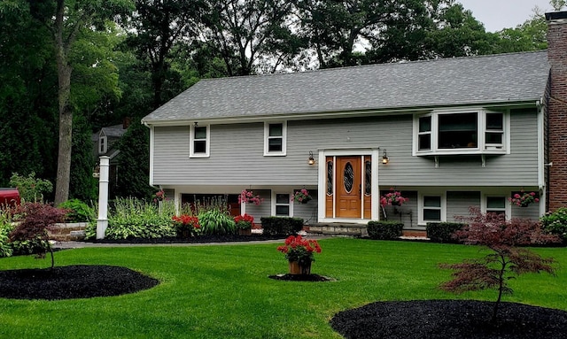 bi-level home with roof with shingles, a chimney, and a front lawn