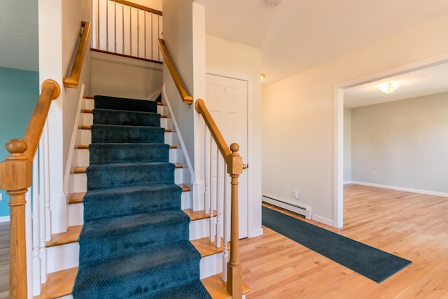 stairway featuring wood finished floors, a baseboard heating unit, and baseboards